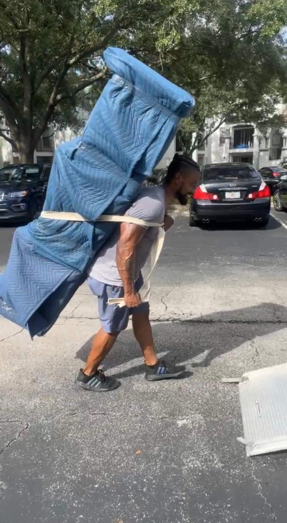 Black Swan Moving mover using a hump strap to carry a large padded item across an apartment parking lot