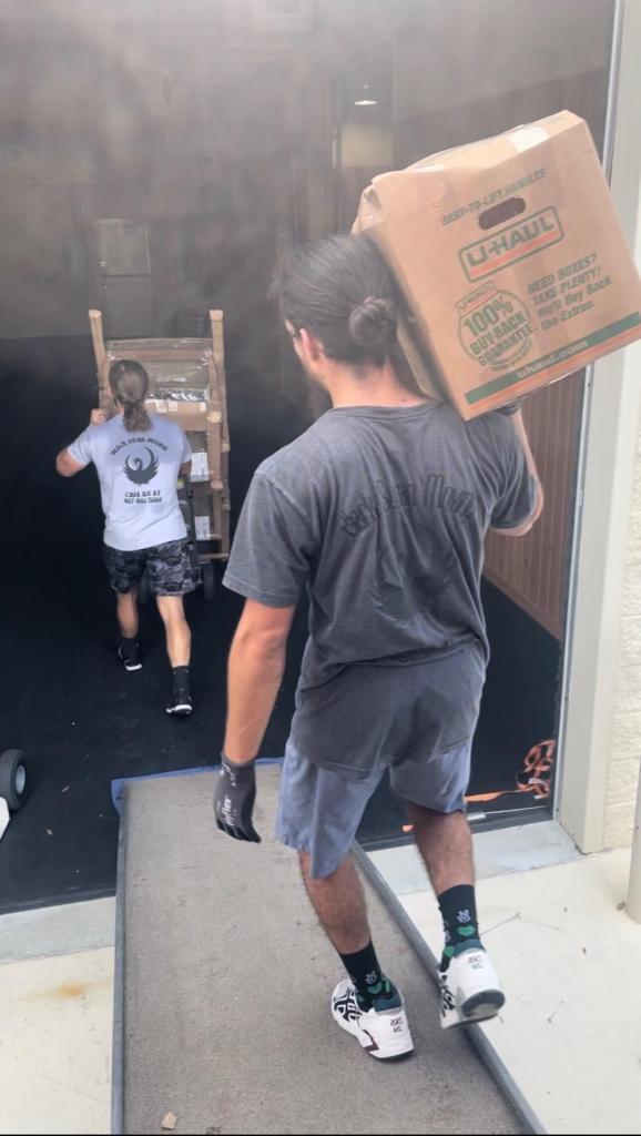 Two movers at work - one with a dolly of patio chairs, the other carrying a box down the truck ramp.
