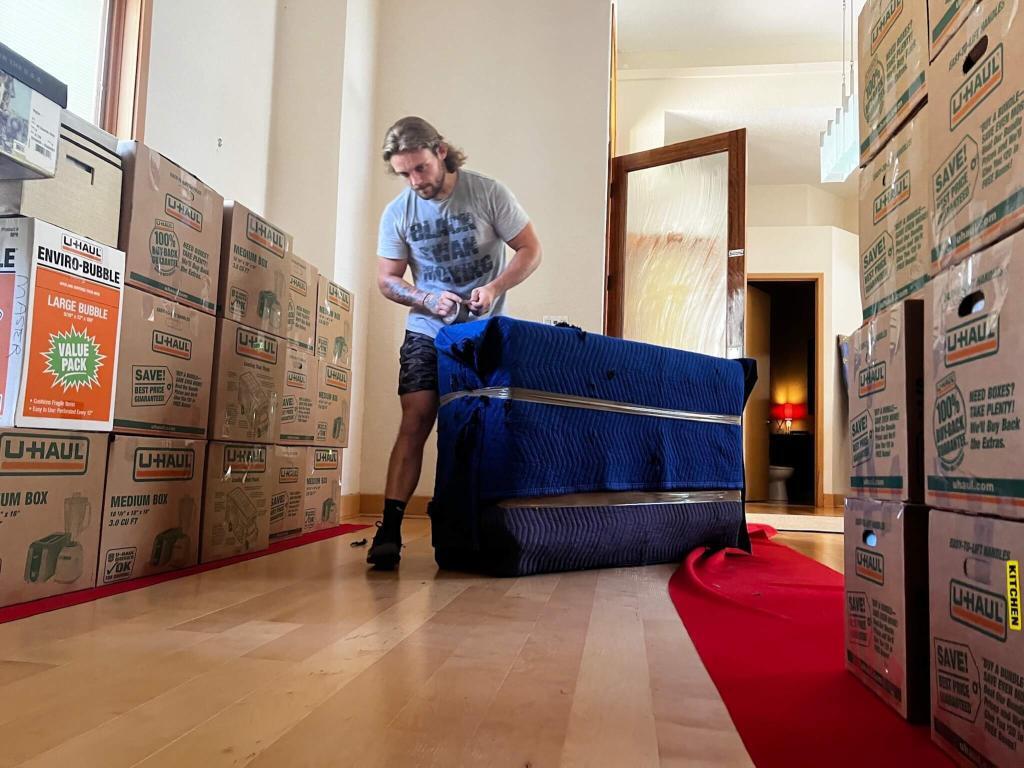 Mover wrapping furniture with a blanket, red carpet floor protection visible.