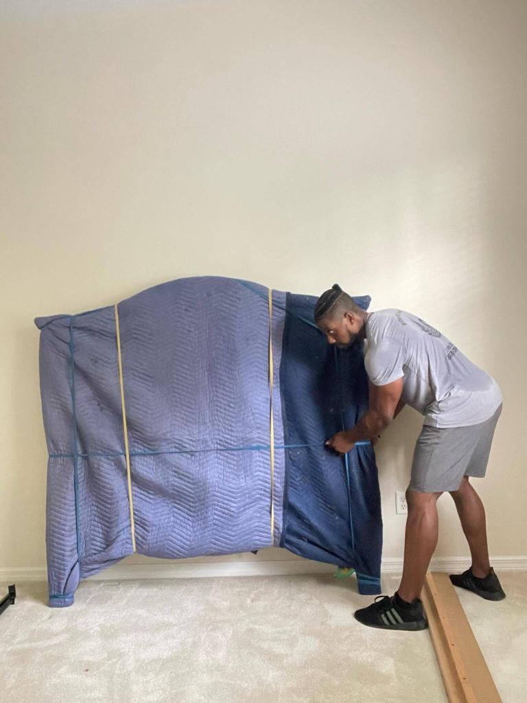 Black Swan Moving | Local & Long Distance Movers in Orange City & Orlando - Black Swan Moving | 5-Star Movers in Central Florida Black Swan Moving mover wrapping a headboard in a blue moving pad before the move