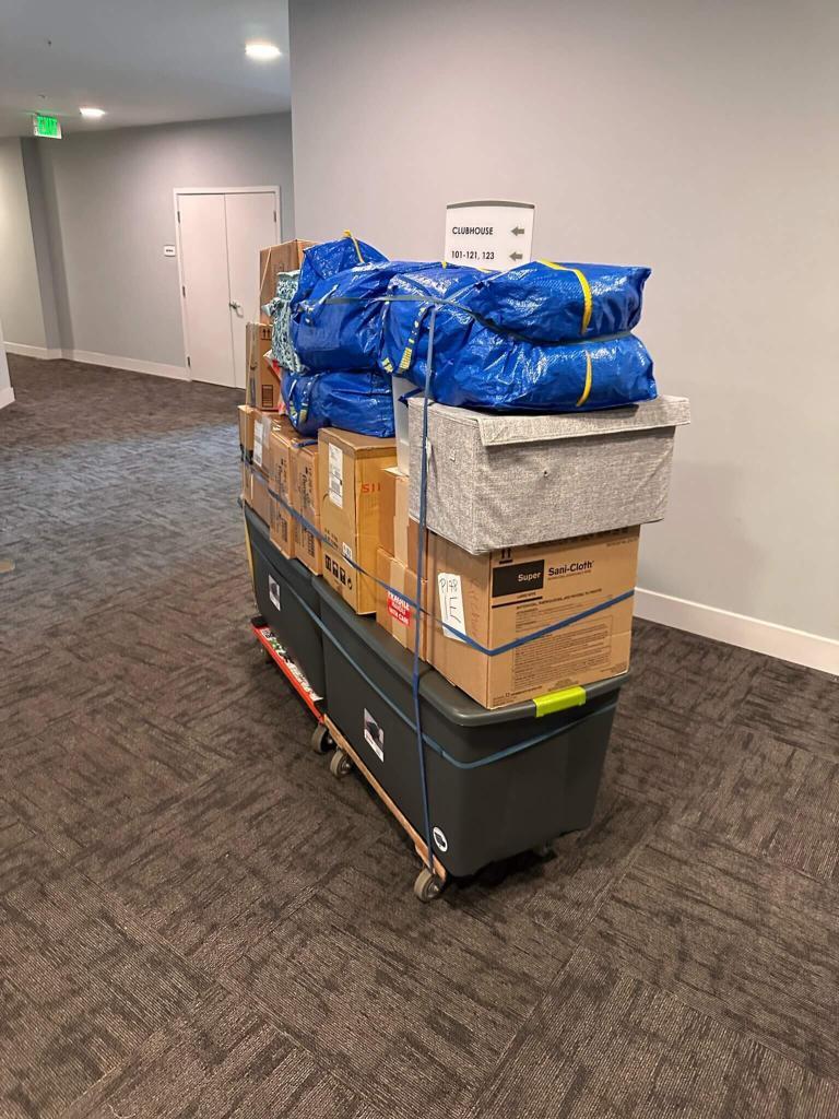 Moving cart stacked with boxes and padded items in a carpeted building hallway