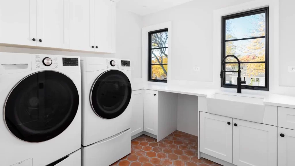 A laundry room with two washers and a sink. The washers are on the left side of the photo, and the sink is on the right side of the photo. Moving appliances.