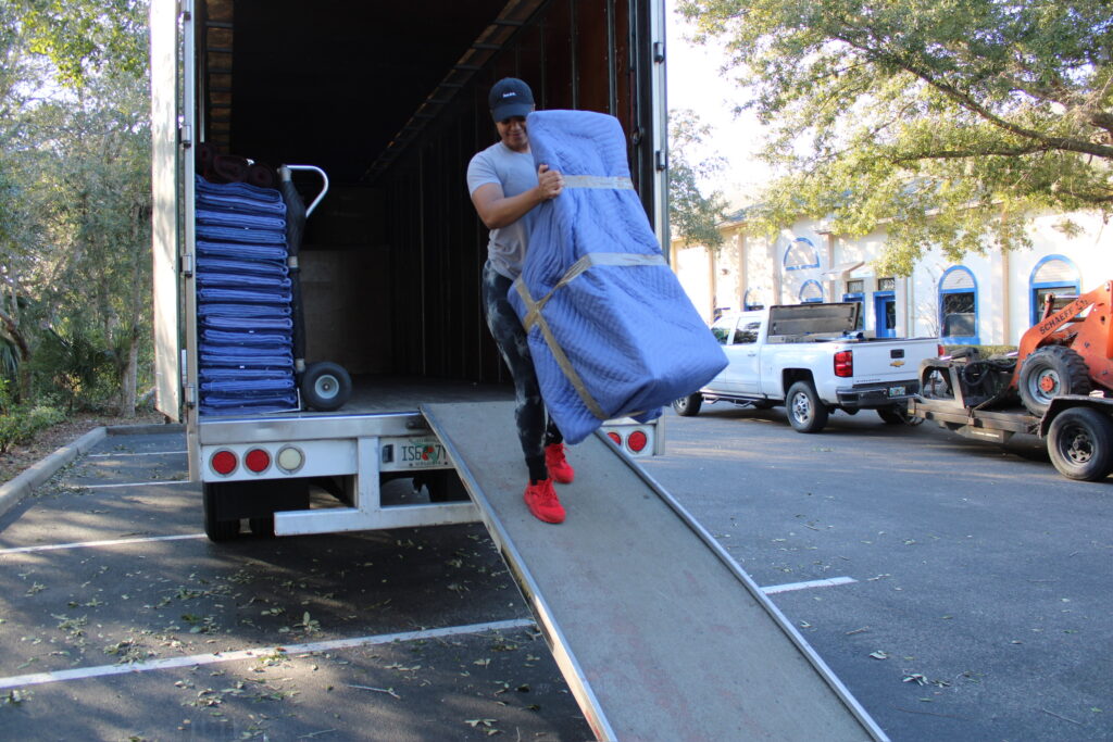 Black Swan mover rolling a blanket-wrapped item down the truck ramp at an apartment complex