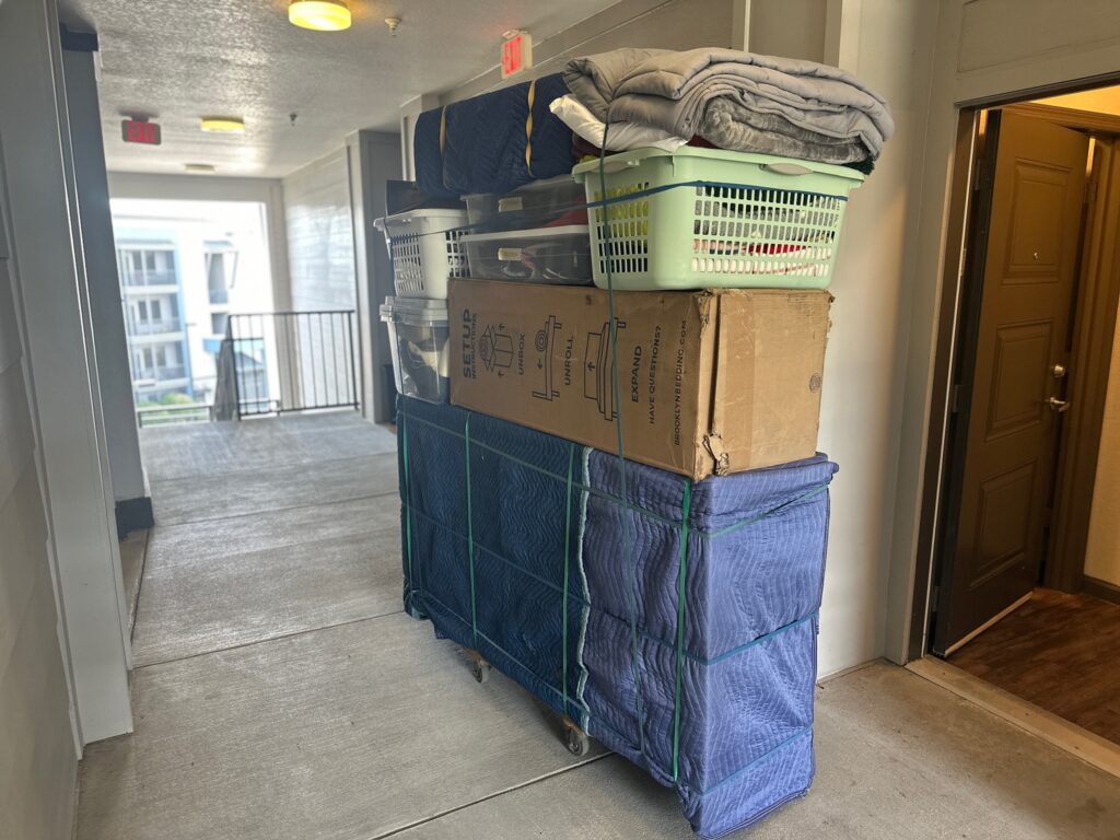 Moving carts loaded with padded furniture and boxes in an open-air condo breezeway during a Black Swan Moving job
