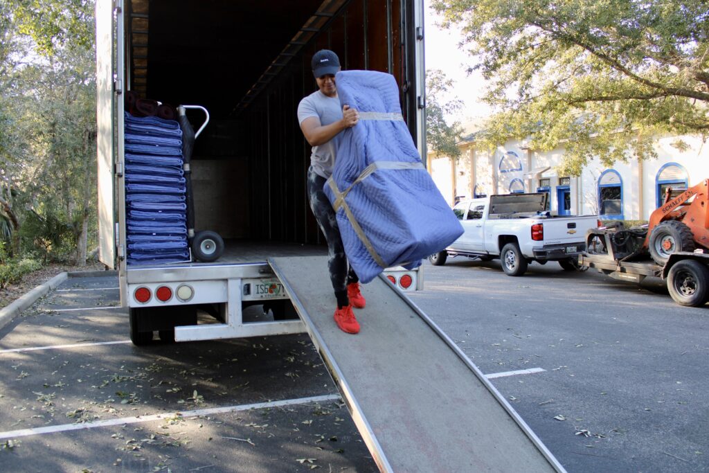 Black Swan Moving crew member carrying a blanket-wrapped chair down a truck ramp