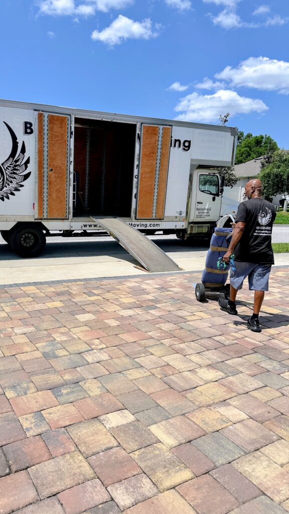 Black Swan Moving truck backed up to a brick paver driveway with the ramp down and a crew member rolling a padded load