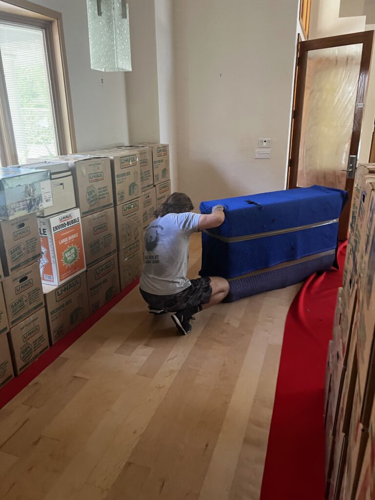Black Swan mover rolling a blanket-wrapped item along a red hallway runner