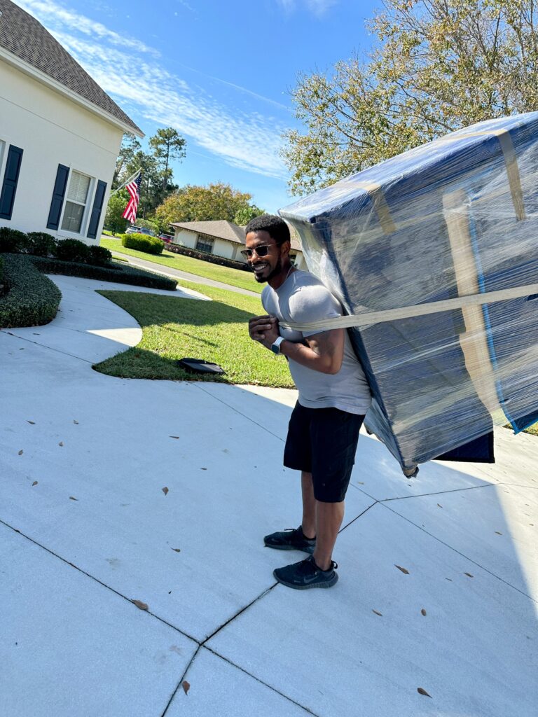 Black Swan mover carrying a blanket-wrapped piece of furniture across a driveway