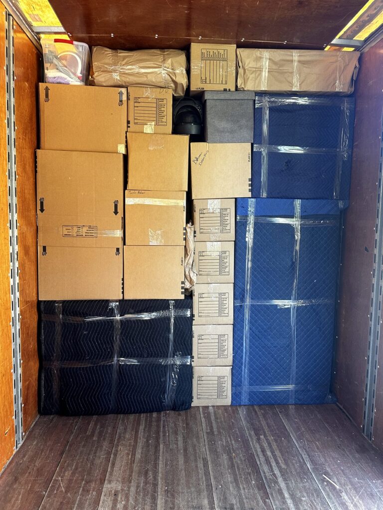 Wall of stacked moving boxes with padded furniture behind it inside the Black Swan Moving truck