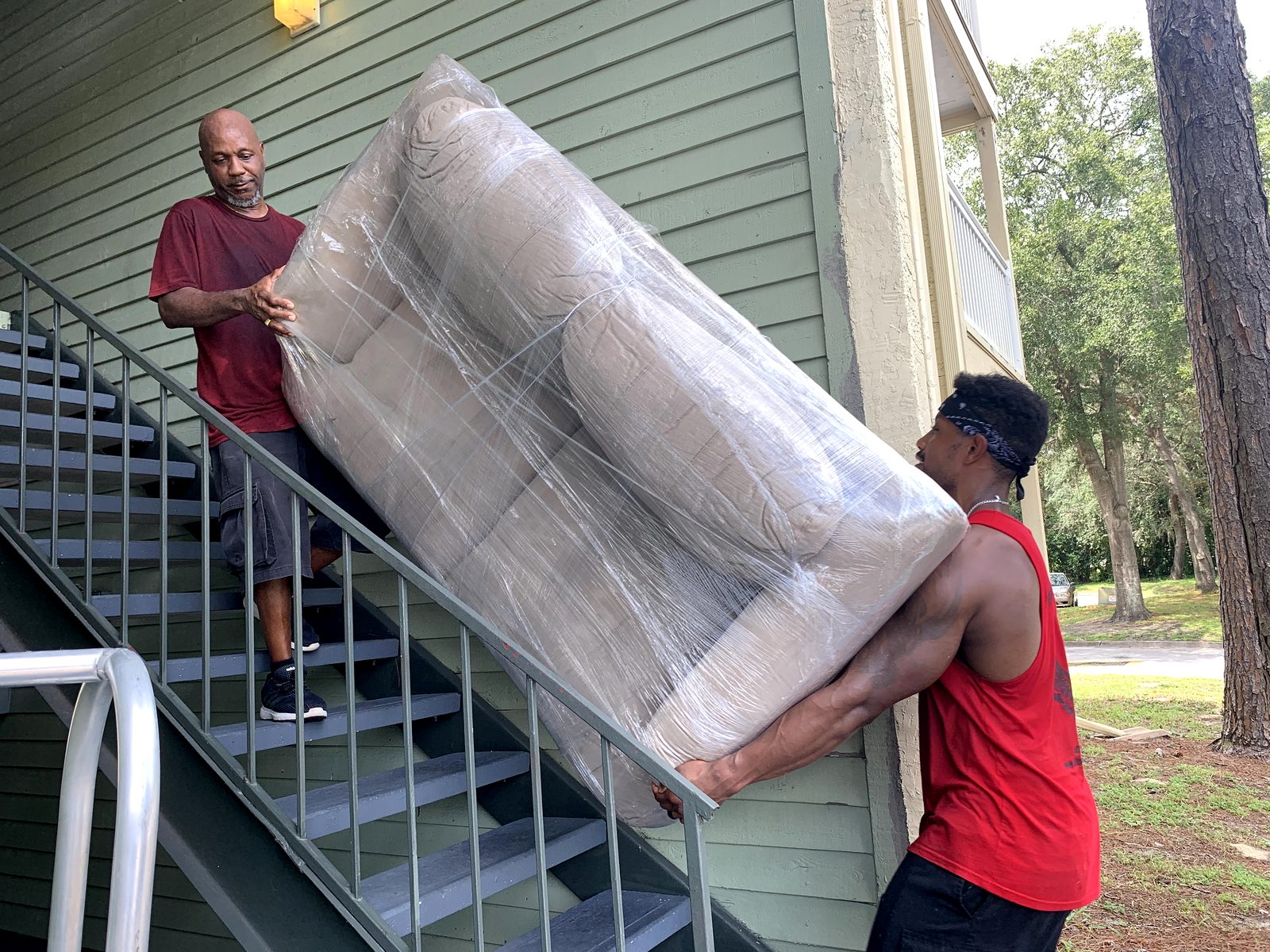 Two Black Swan Moving crew members carrying a shrink-wrapped loveseat down apartment stairs