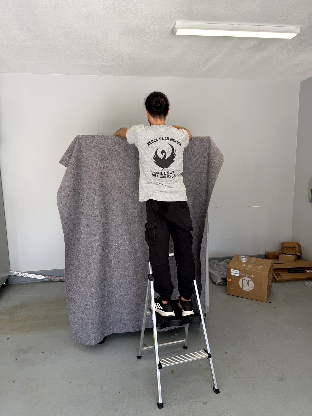 Black Swan Moving crew member on a step ladder padding a tall piece of furniture