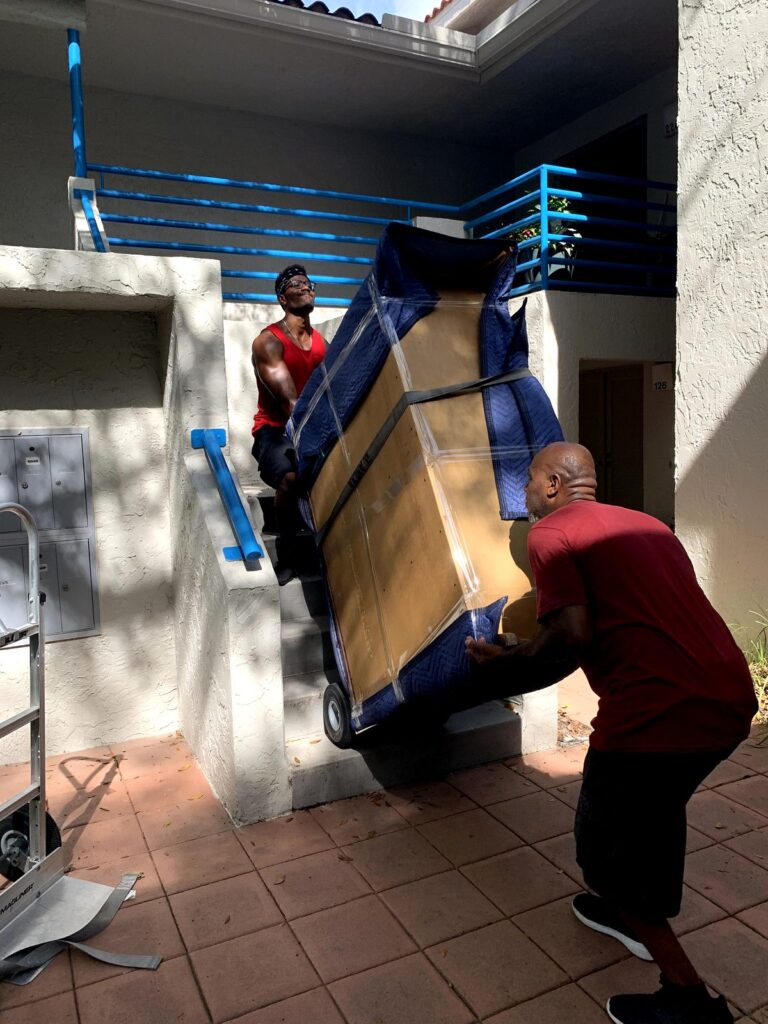 Black Swan Moving | Local & Long Distance Movers in Orange City & Orlando - Black Swan Moving | 5-Star Movers in Central Florida Two Black Swan Moving crew members tilting a fully padded hutch onto a dolly