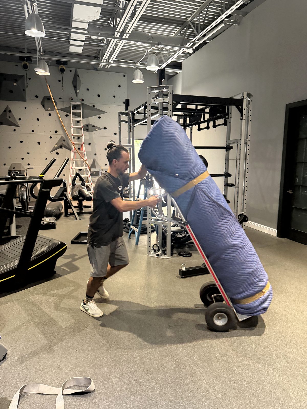 Black Swan Moving crew member rolling padded gym equipment on a hand truck through a fitness studio