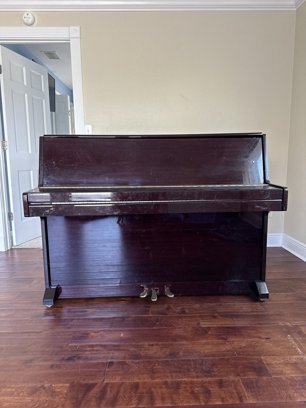 Dark wood upright piano standing against a wall on a hardwood floor before Black Swan Moving wraps it