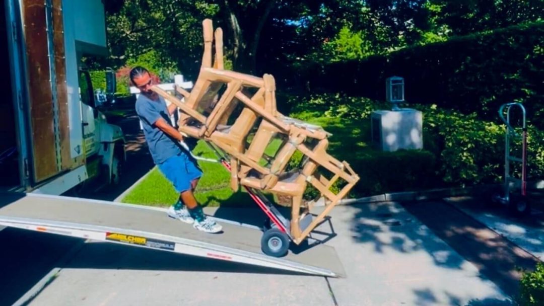 Mover with dolly loading patio chairs onto the Black Swan Moving truck.